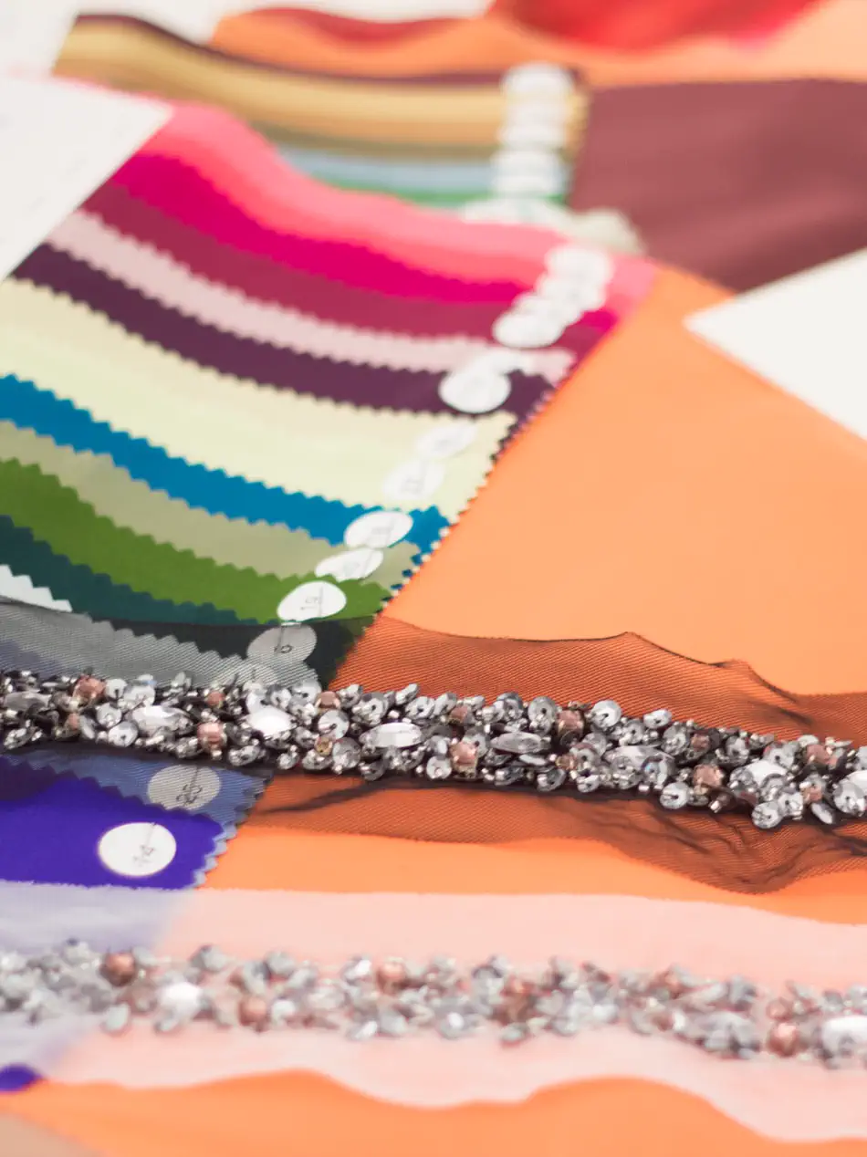 A fanned colour card beside crystal and sequin trims laid across a sheet of orange silk