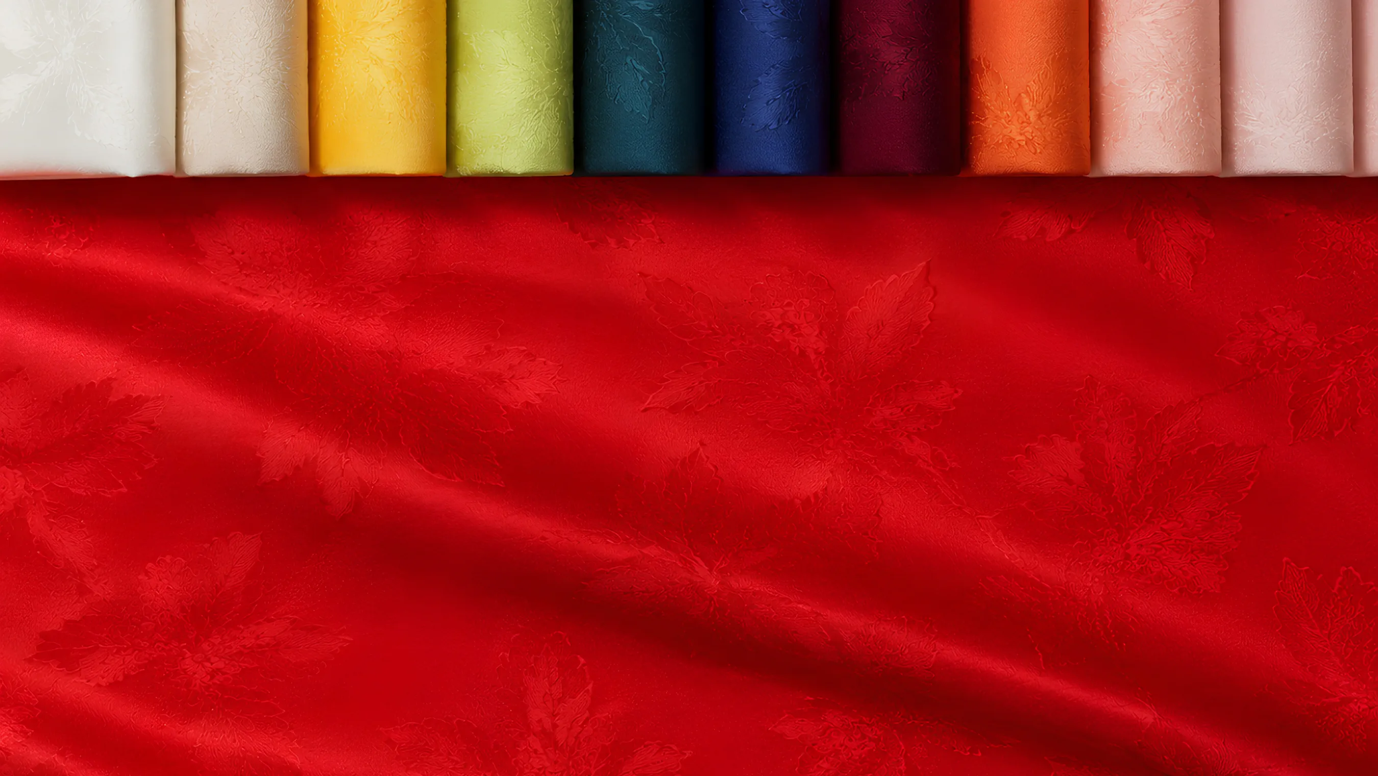Red damask woven with a leaf motif, below a row of rolled bolts running the full colour range