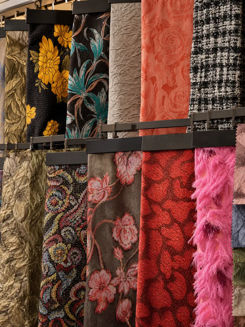 Rails of hanging fabric samples in the showroom — brocades, jacquards, tweeds, and fringing